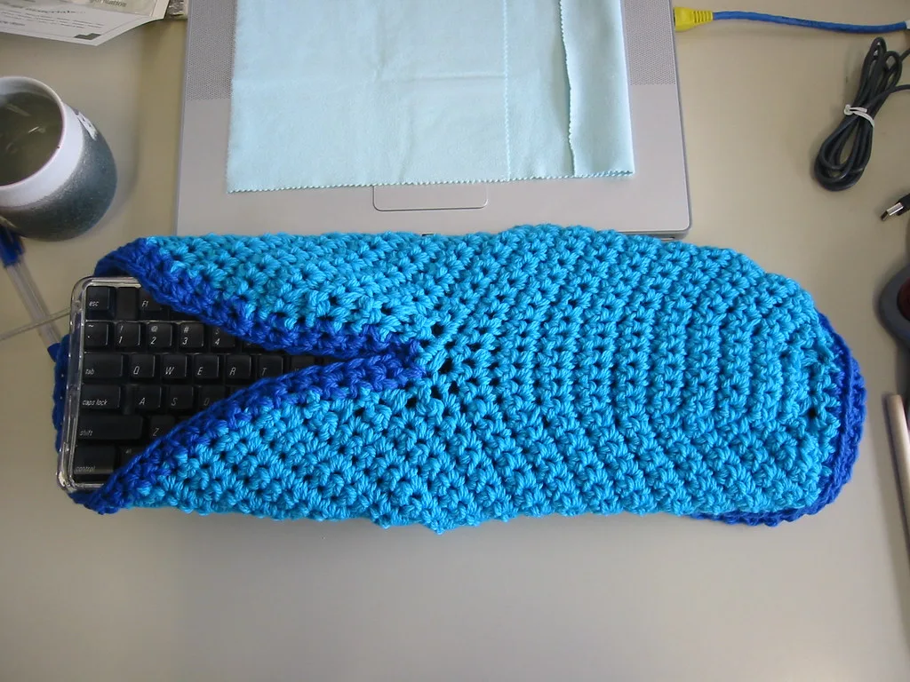 A crocheted wool boot slipper before fulling, larger than the keyboard beside it