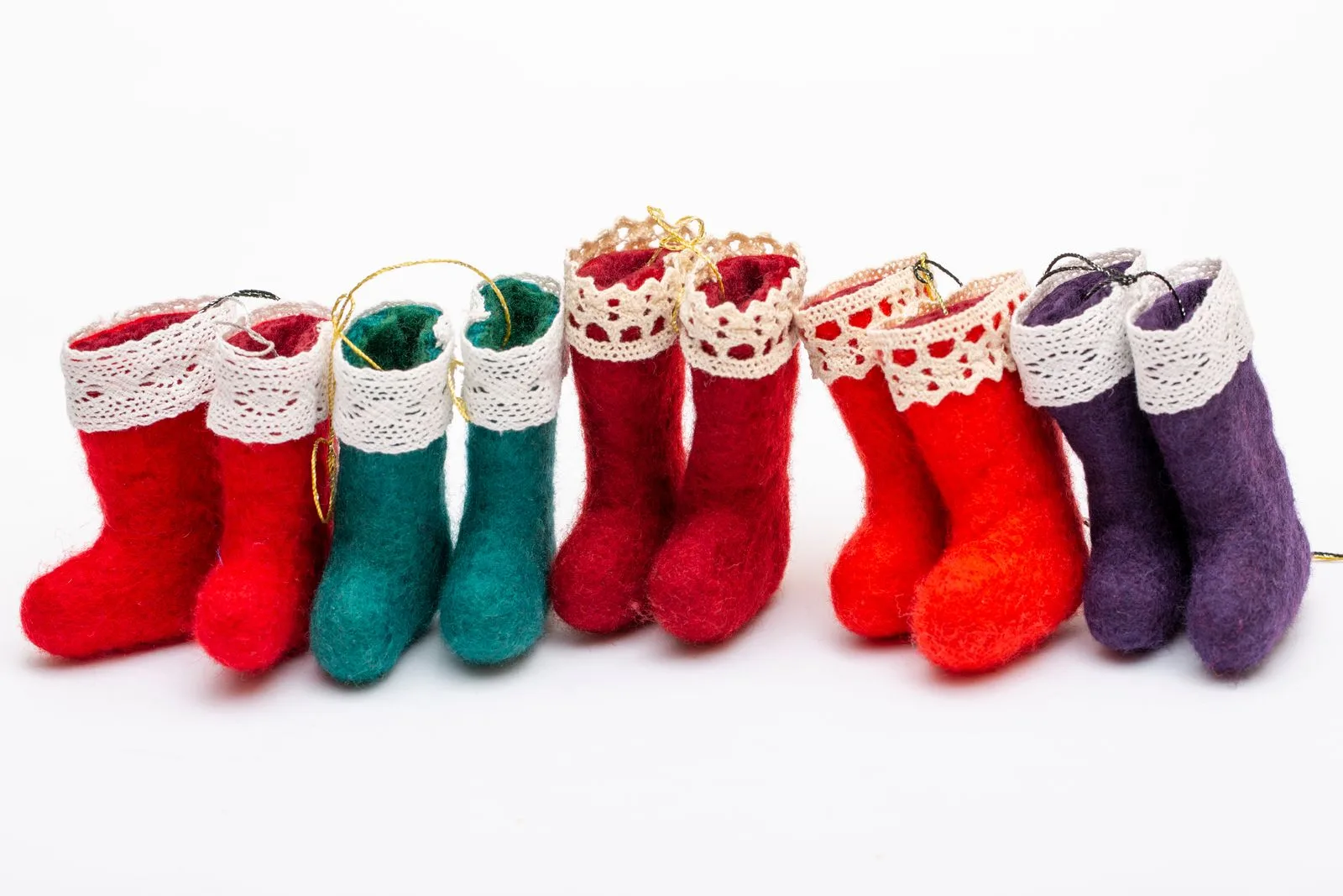A row of small felted boot ornaments in red, teal and purple with lace cuffs and hanging loops
