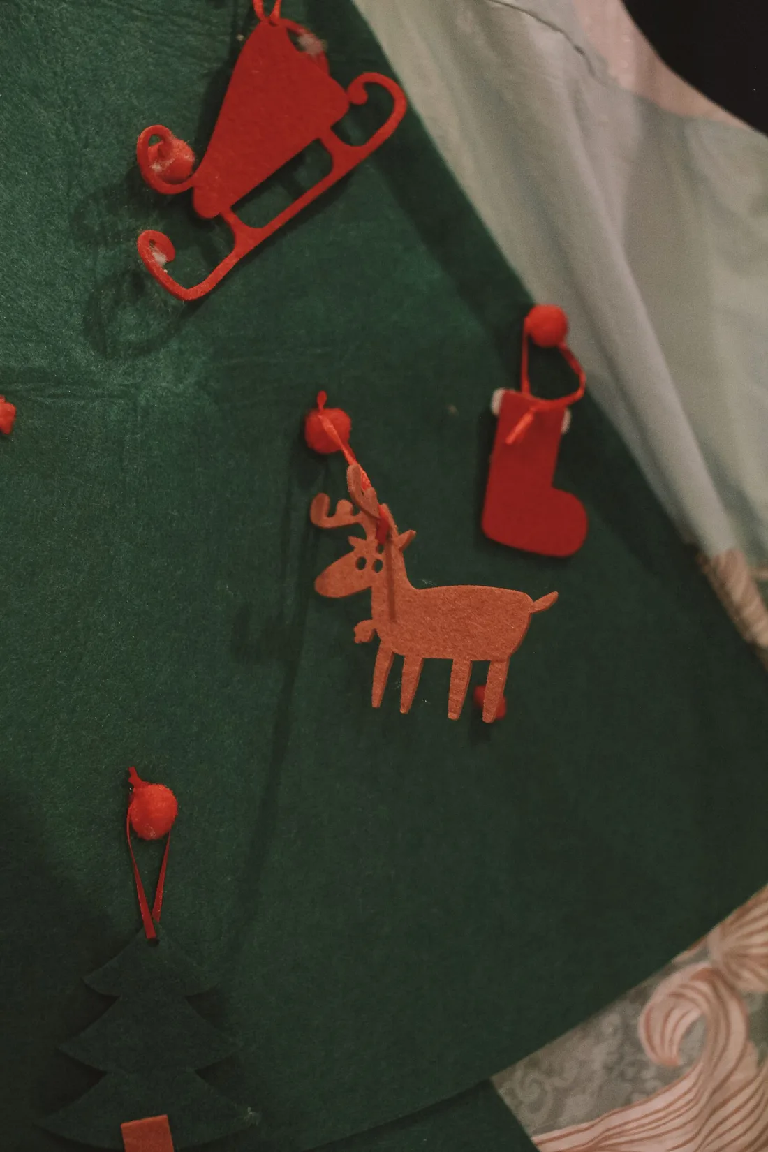 A green felt wall tree with a felt sleigh, reindeer and stocking hung by ribbon loops from small red pompoms