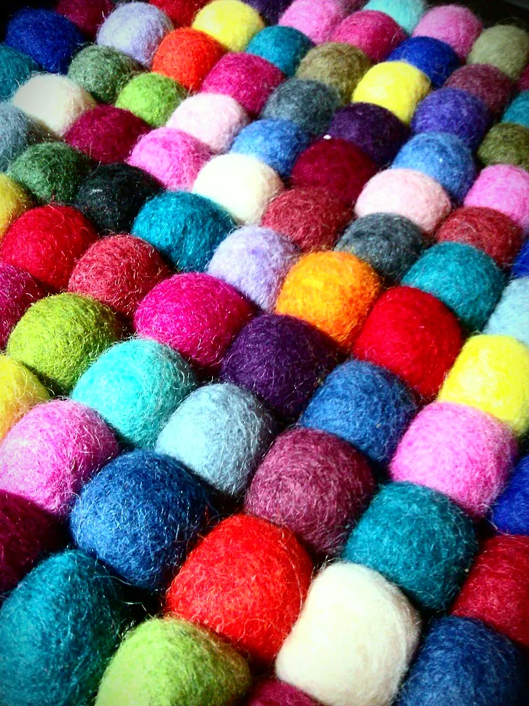 A felt ball coaster in bright colors, with the wool balls set in straight diagonal rows