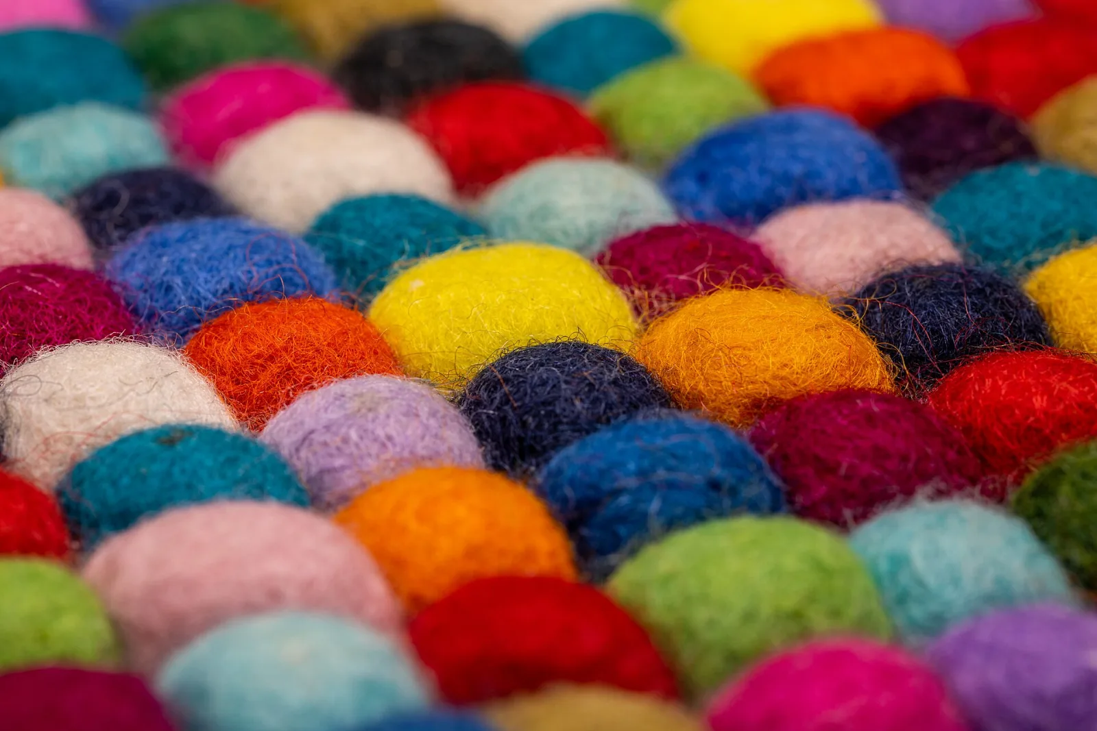 Close-up of a felt ball coaster made from multicolored wool balls sewn tightly together