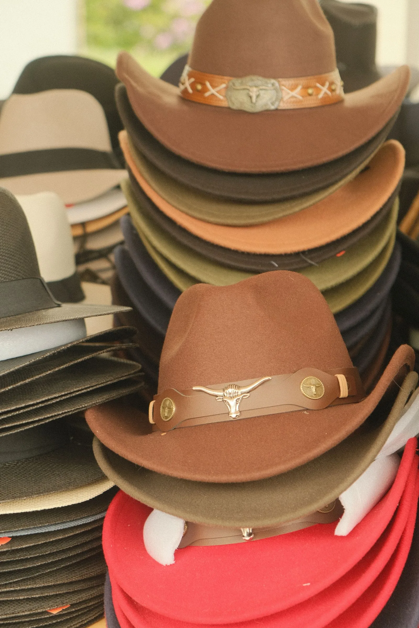 Stacks of felt cowboy hats in brown, olive, black and red, two with leather bands and longhorn badges