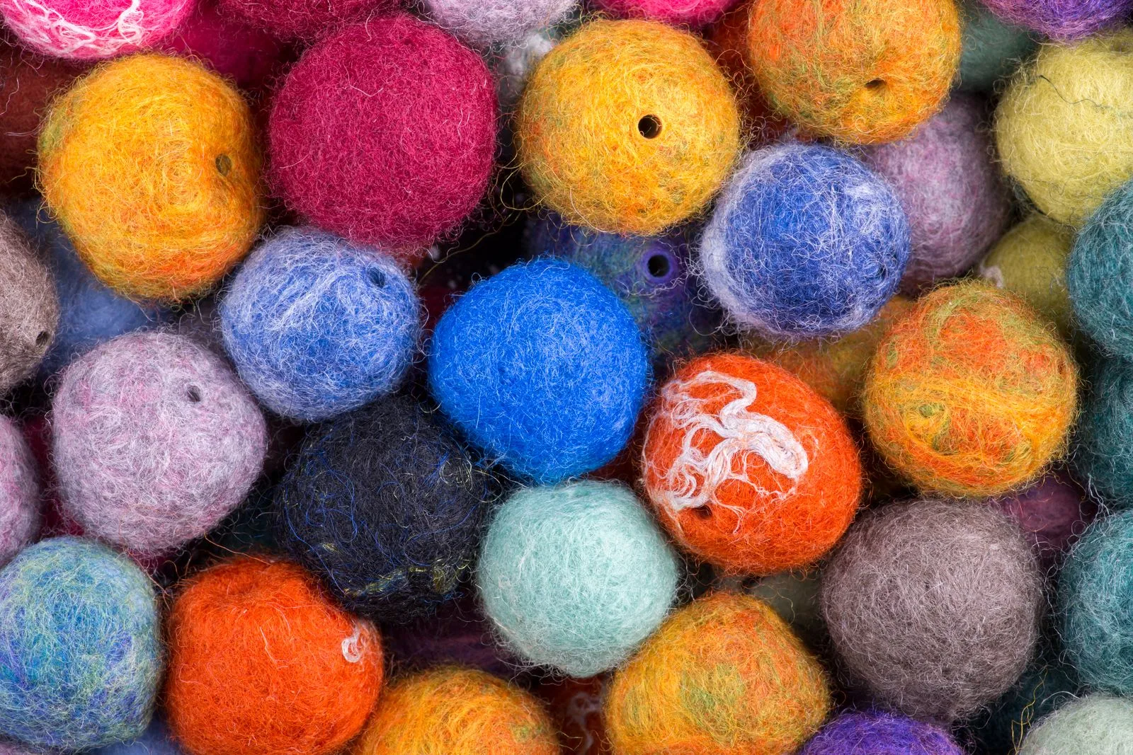 A heap of multicolored wool felt balls, several already pierced through the middle for stringing
