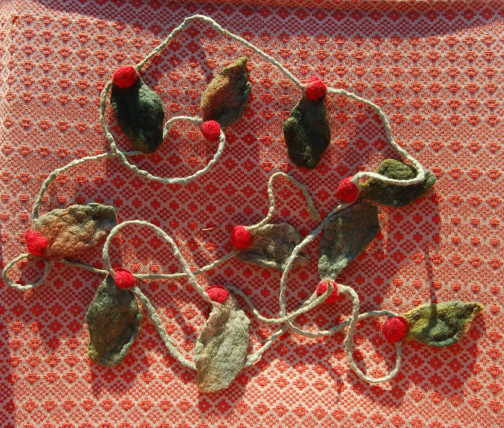 A wet felted garland of green felt leaves and red felt berries strung along a twisted cord