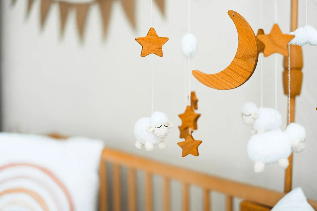 A mobile of crocheted white sheep, wooden stars and a wooden crescent moon on an arm clipped to a wooden crib