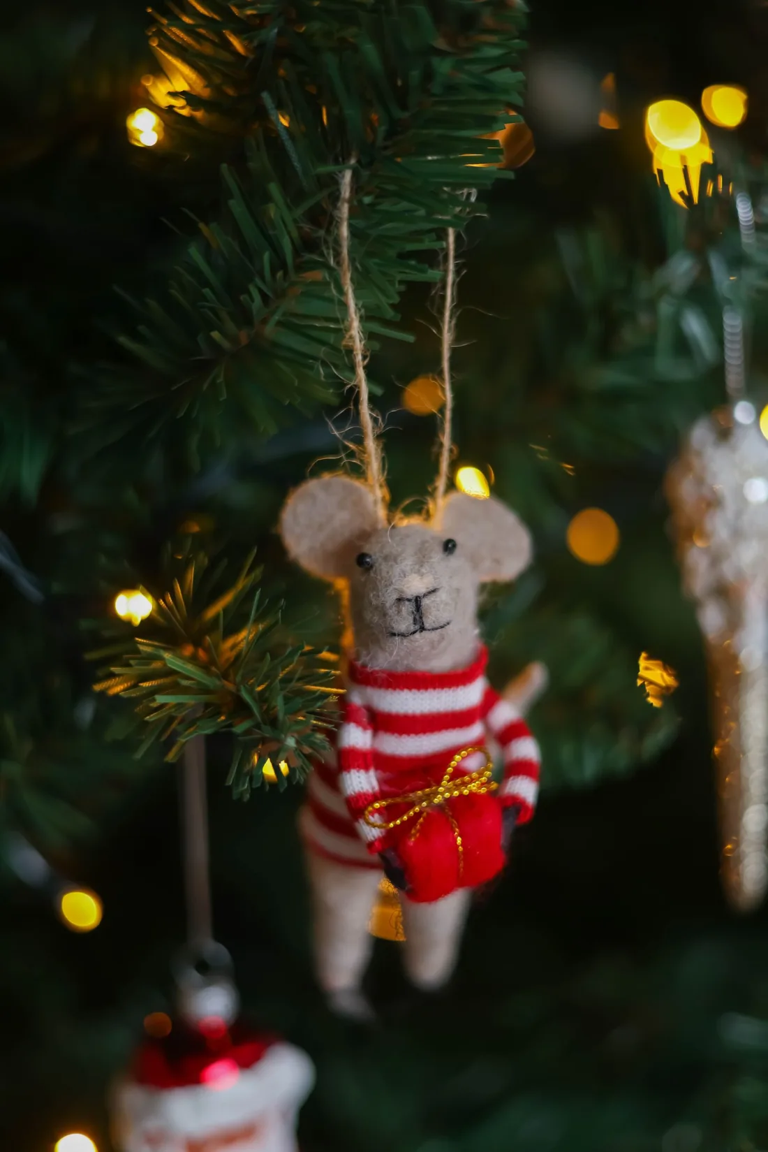 A needle felted mouse ornament in a striped jumper hanging on a Christmas tree