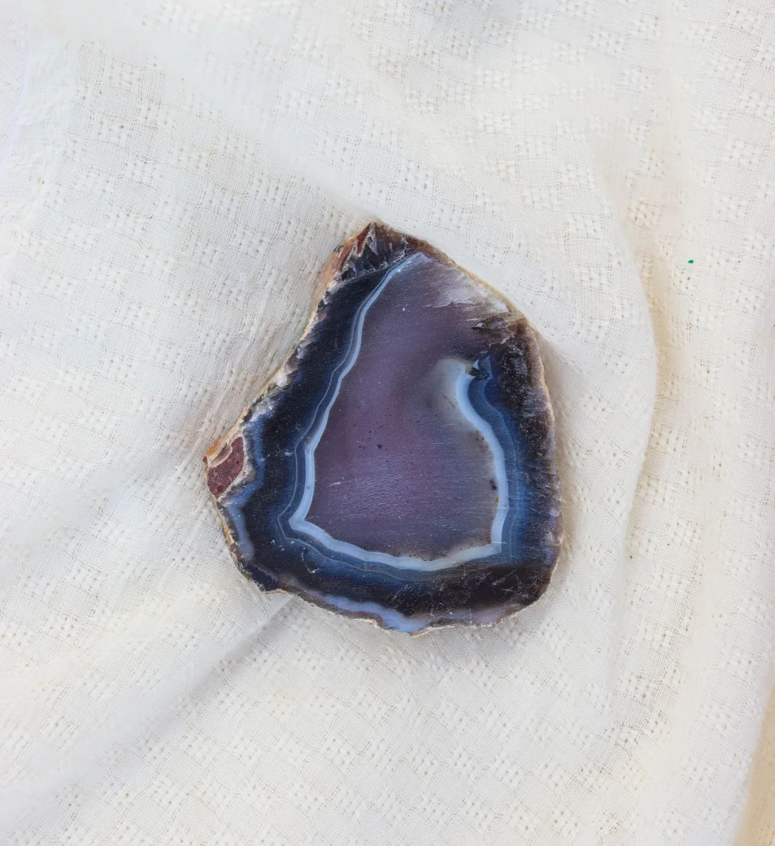 A polished slice of agate with bands of blue, purple and grey, lying on white cloth