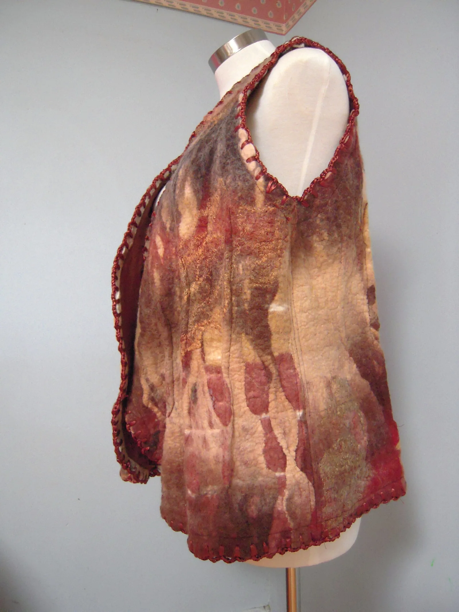 A handmade felted vest in warm reds, golds and browns displayed on a dress form