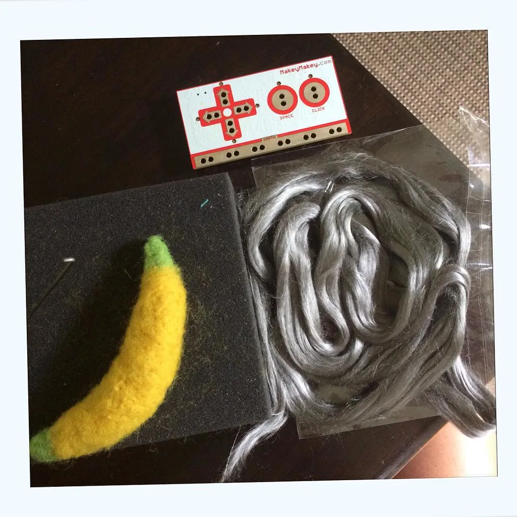 A needle felted piece and wool roving on a black foam felting pad