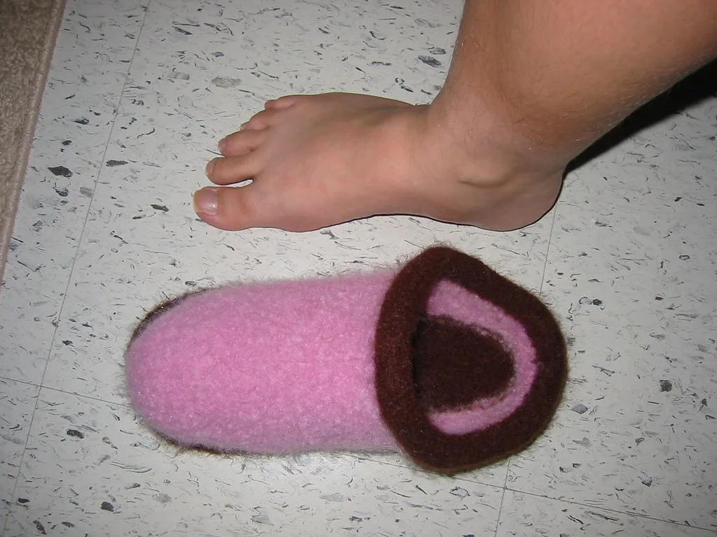A knitted clog after felting, beside a bare foot for scale