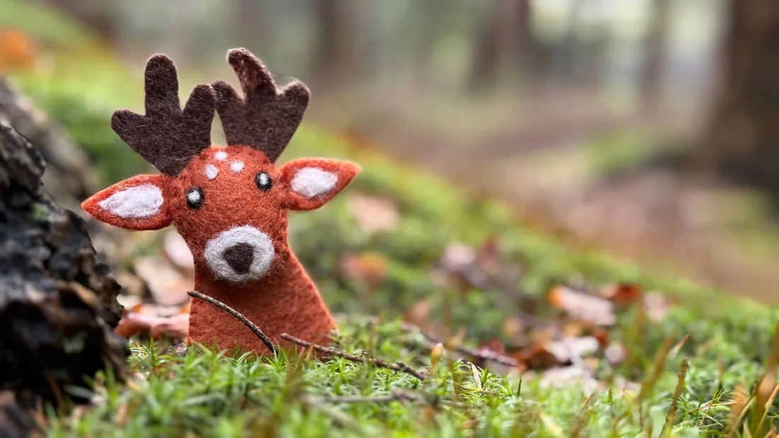 A felt deer finger puppet held up among autumn leaves