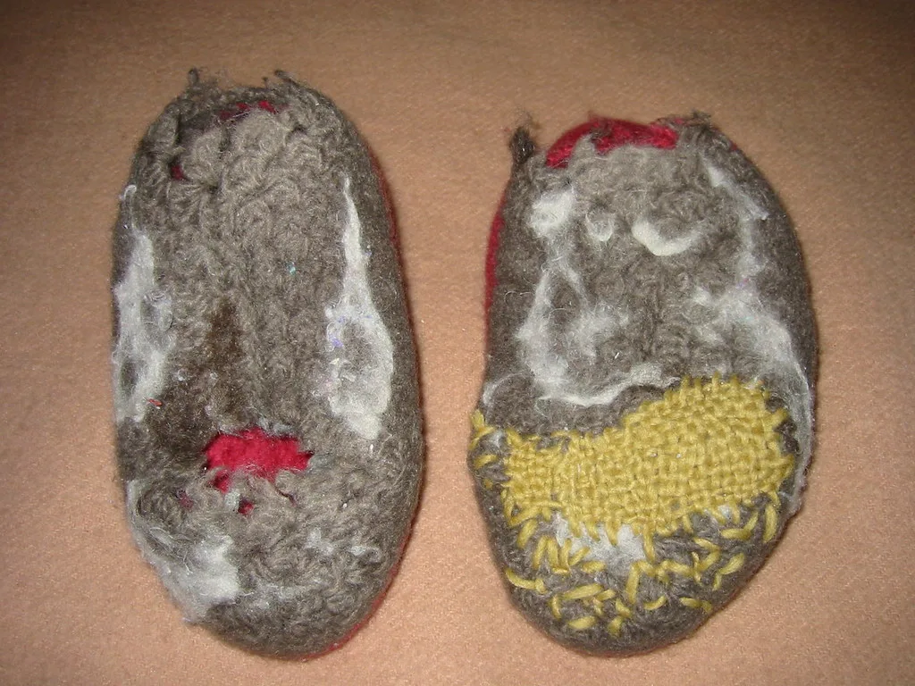 The undersides of two worn slippers, one worn through and one darned