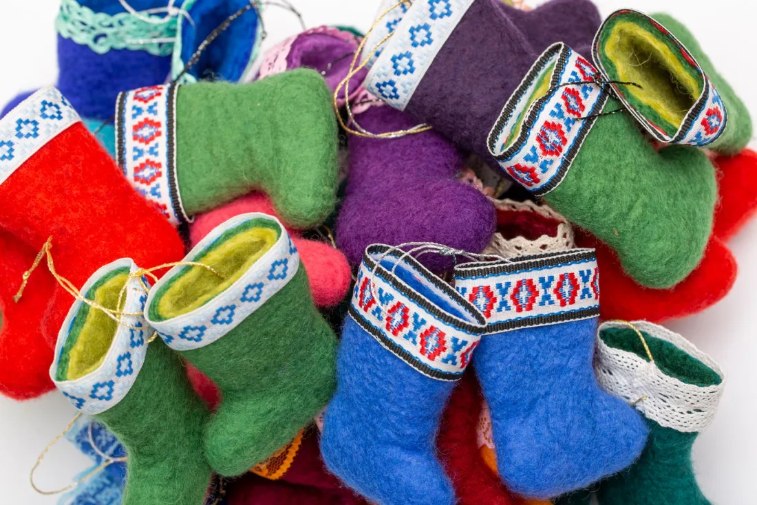 A pile of miniature felted valenki ornaments in red, green, blue and purple with woven ribbon cuffs