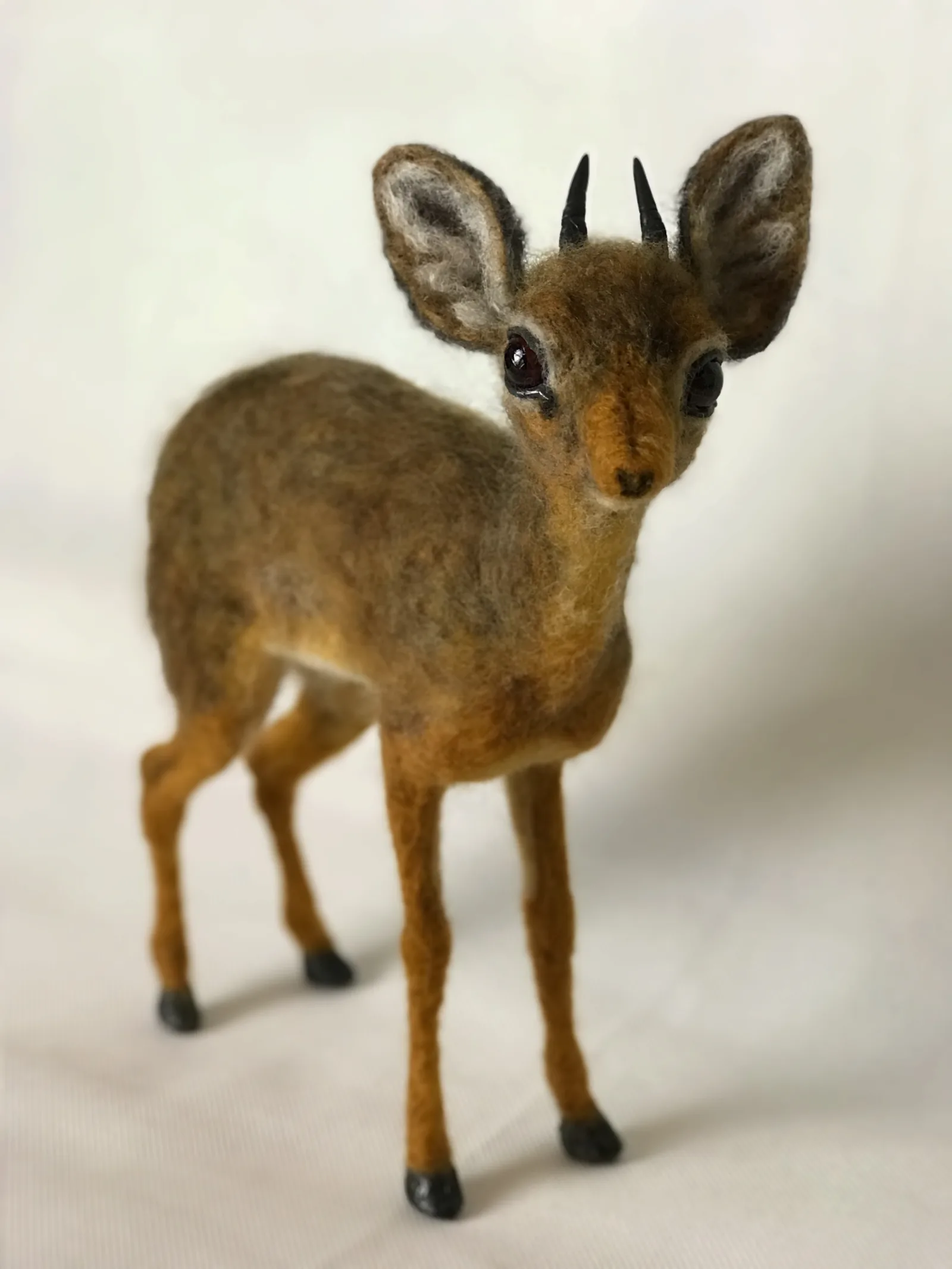 A needle felted animal standing on thin legs over a wire armature
